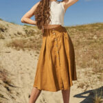 Woman wearing yellow-beige, flowy, linen skirt reaching just under her knees and with row of small wooden buttons halfway down.