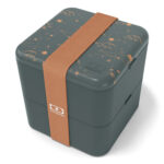 Dark-green, plastic cube-shaped lunchbox with gold colored, subtle shooting star designs on the lid and gold broad elastic band.