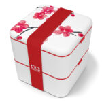 White, plastic cube-shaped lunchbox with Japanese-style flowers on the lid and red broad elastic band.