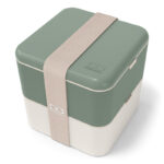 Plastic cube-shaped lunchbox with russian green upper hald, white lower half and light-purple broad elastic band.