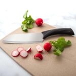 Medium-sized cook's knife with black plastic handle lying on a cutting board beside cut radishes.