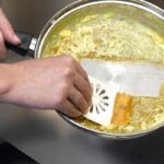 White panmate scraper being used to scrape burnt mashed potatoes off steel frying pan.