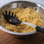 Pasta server lying in a bowl of cooked spaghetti.