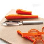 Straight peeler with swivel blade and aluminum handle lying beside peeled carrots.