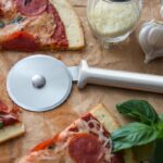 Pizza cutter with round, rolling blade and aluminum handle lying on a pizza.