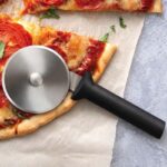 Pizza cutter with round, rolling blade and black plastic handle lying on a pizza.