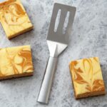 Small spatula with aluminum handle and two slots in the face, lying beside pieces of cake.