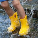 Kid jumping in puddle waering yellow rain boots