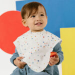 Young toddler wearing white bib with colored dots while eating a strawberry