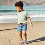 Child at the beach wearing blue shorts with orange drawstring and green t-shirt with front pocket.