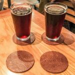 Two beer glasses on top of salmon leather coasters