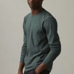 Sideview of man wearing green, longsleeve t-shirt with front pocket.