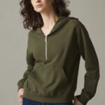 Woman wearing dark green hoodie with big front pocket and zipper at the neckline.