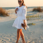 Woman at the beach wearing white top with three-quarter puff sleeves.