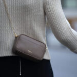 Woman carrying small brown leather purse on chain shoulder strap.