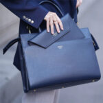 Woman carrying large blue leather handbag with small purse in its side compartment.