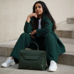 Woman sitting with dark green leather handbag.