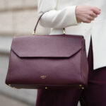 Woman carrying dark red leather handbag on arm.