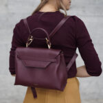 Woman carrying dark red leather handbag as backpack.