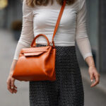 Woman carrying orange handbag with shoulder strap.