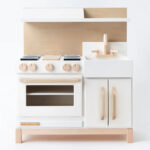 White wooden play kitchen with oven, stove, hood and sink.